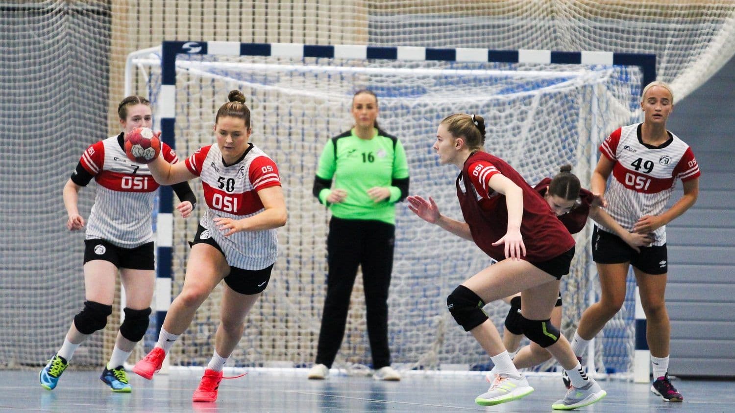 Håndballkamp mellom to lag, der spillere i OSI-drakter angriper mot målet.