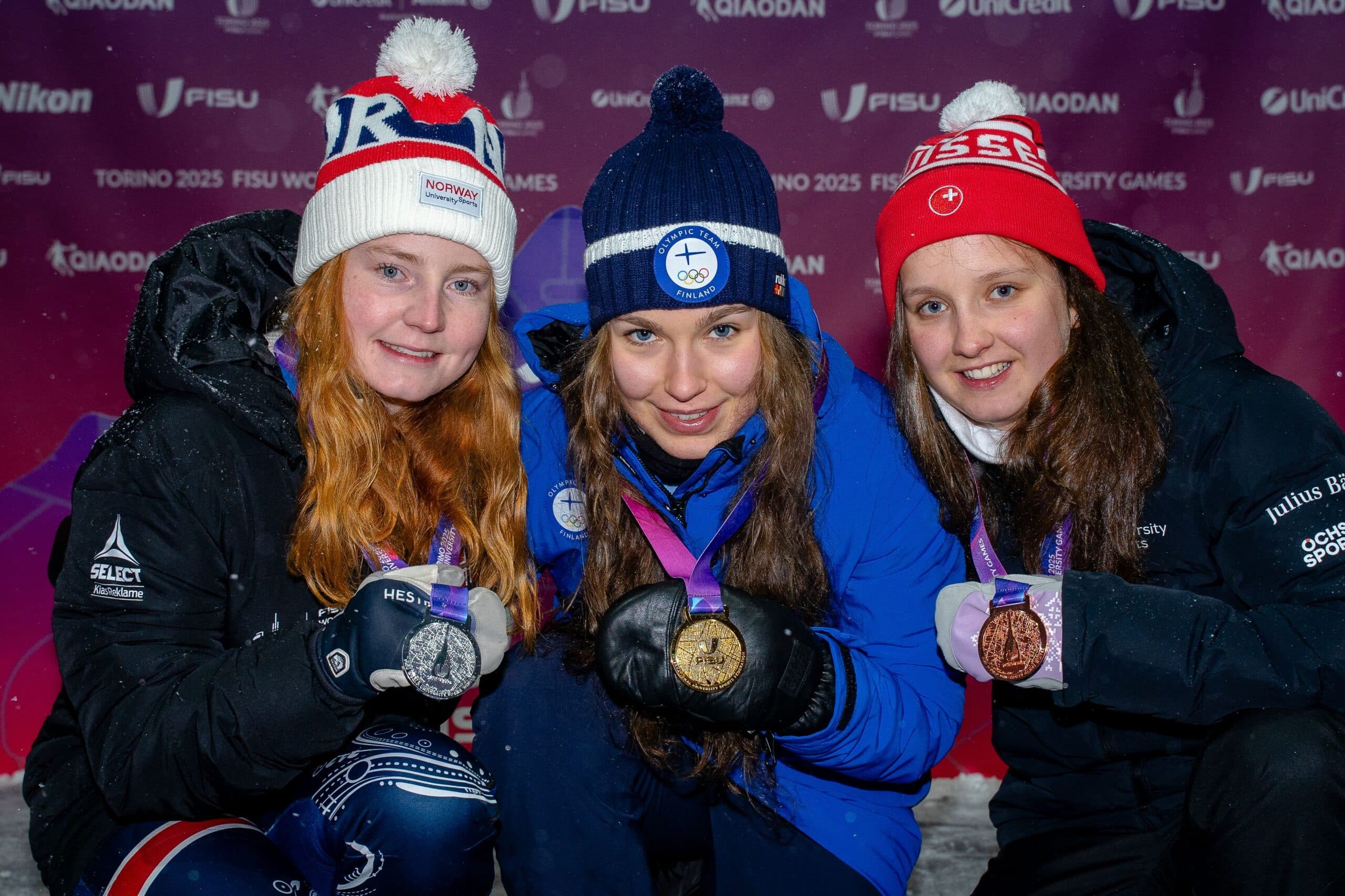 Tre kvinnelige utøvere med medaljer poserer sammen under FISU World University Games Torino 2025.