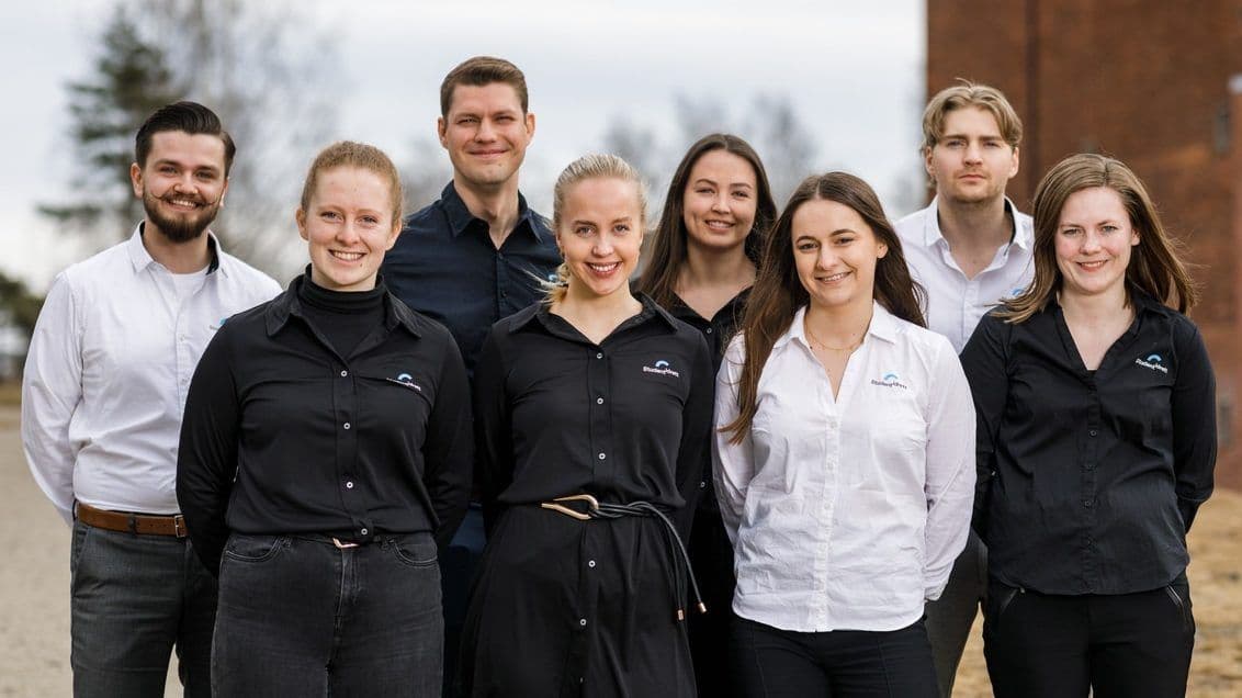 Åtte personer i sorte og hvite skjorter poserer samlet utendørs som en gruppe.
