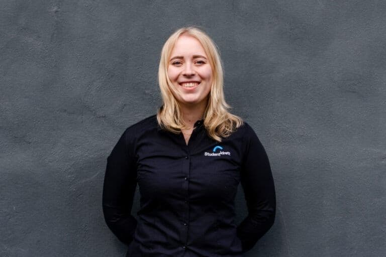 Portrett av en smilende kvinne i svart skjorte foran en grå vegg.