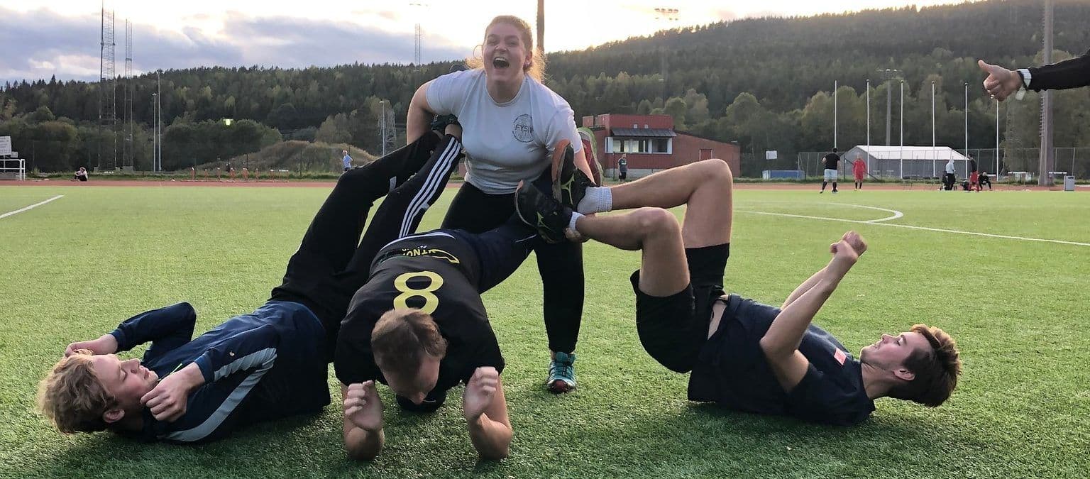 En leende gruppe studenter ligger og henger sammen på en fotballbane etter trening.