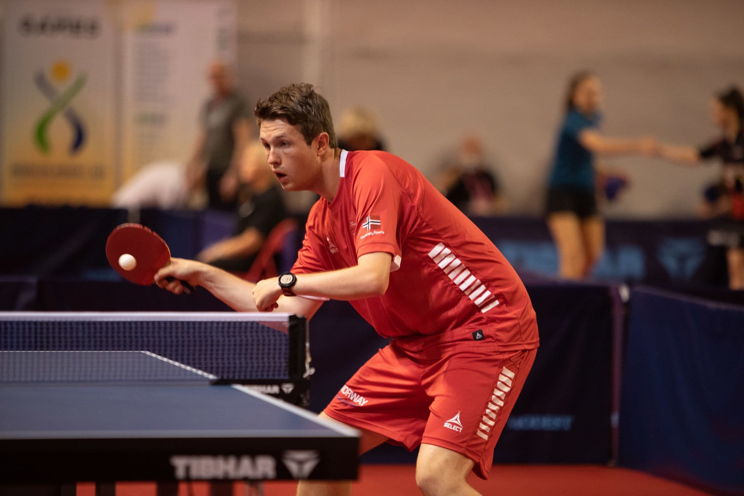 En bordtennisspiller i rødt server ballen under en kamp.