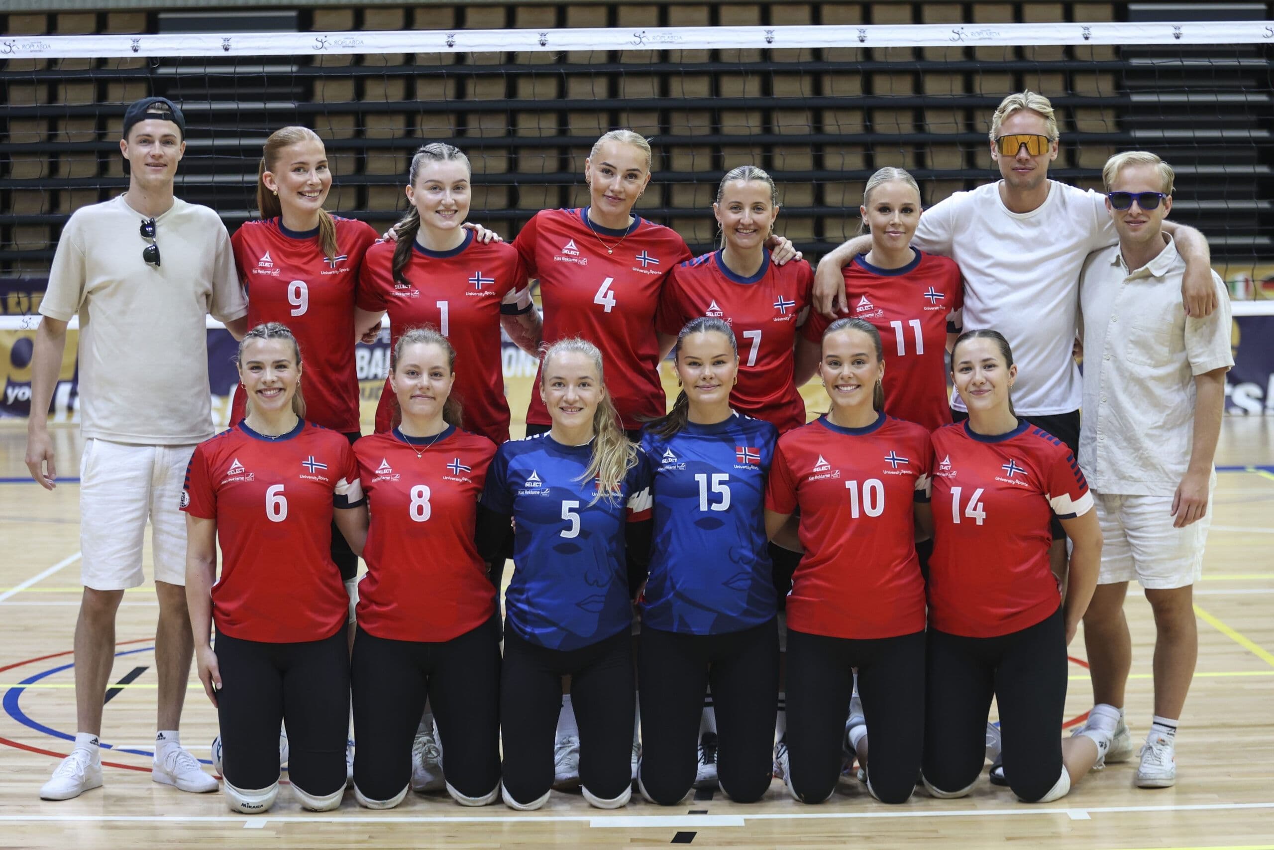 Et volleyballag i røde og blå drakter poserer samlet i en idrettshall.