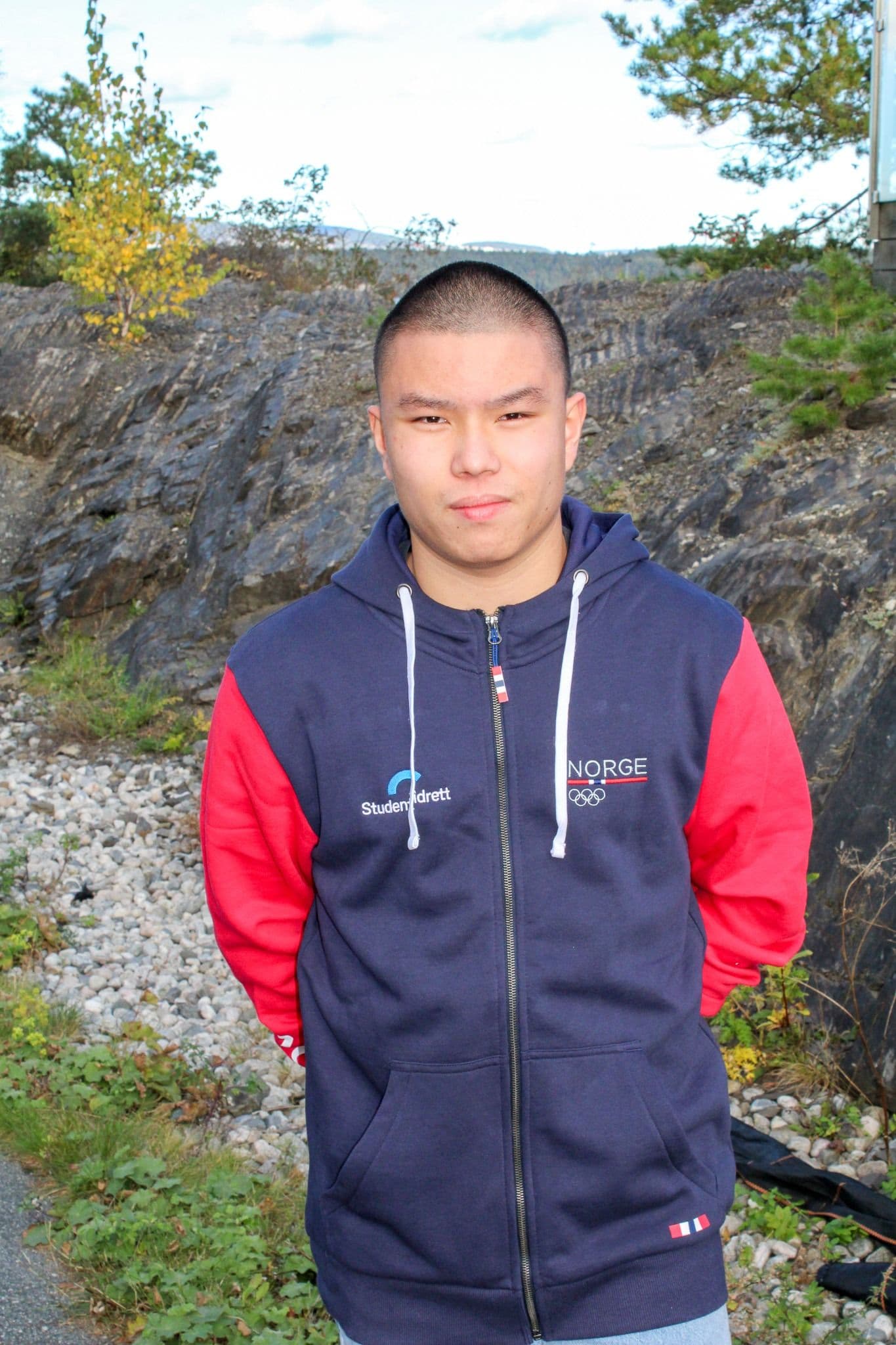 Portrett av en ung mann i marineblå jakke med Studentidrett- og Norge-logo, ute i naturen.