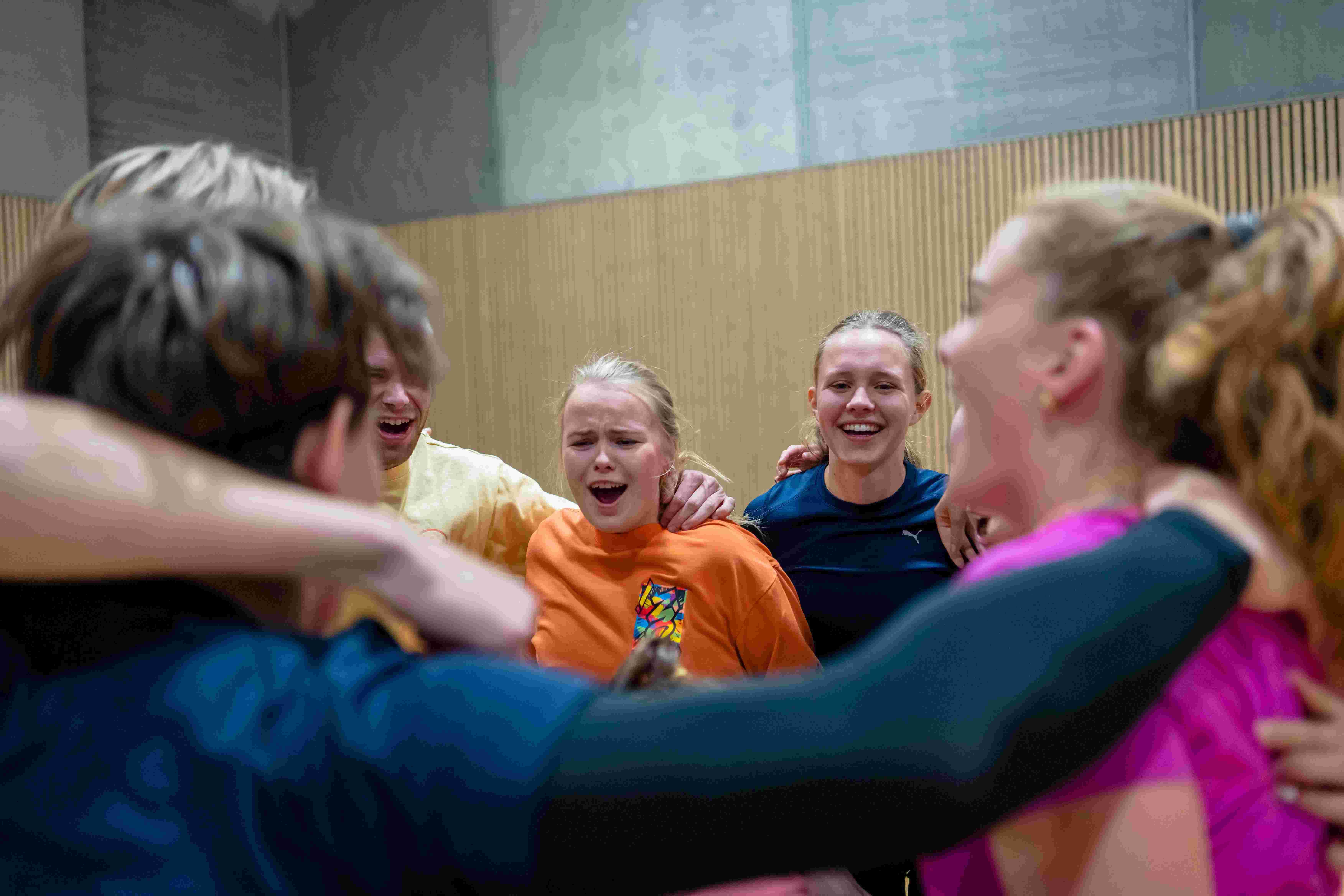 En gruppe studenter jubler og omfavner hverandre i en idrettshall.