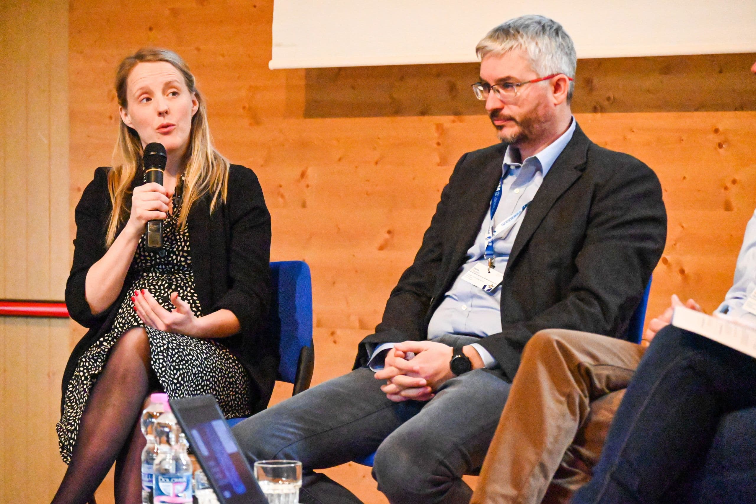 En kvinne snakker i mikrofon ved siden av en mann under en paneldebatt.