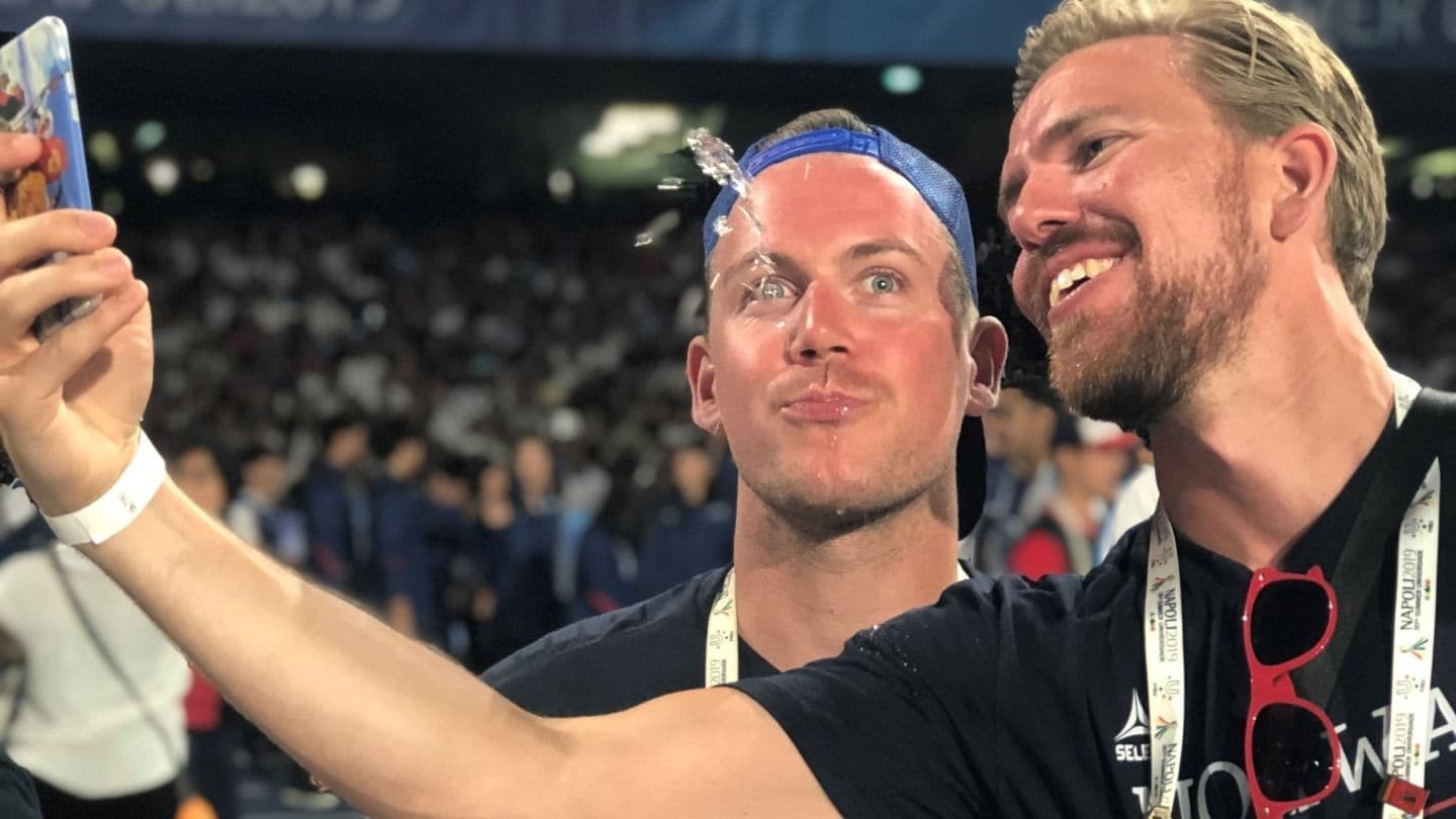 To menn tar en selfie på en stadion med fulle tribuner i bakgrunnen.
