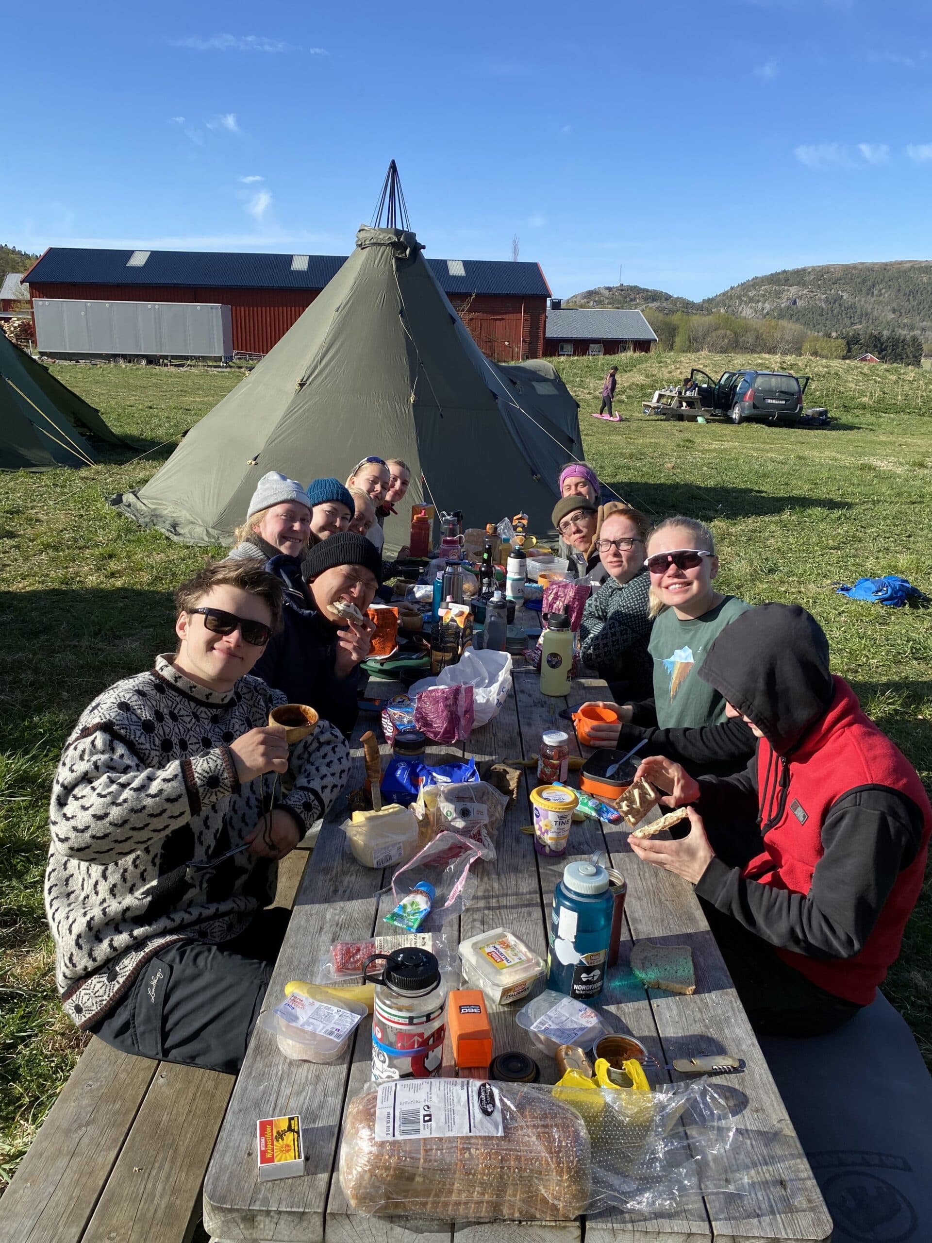 En gruppe studenter samlet rundt et langbord ute foran en lavvo på en solrik dag.