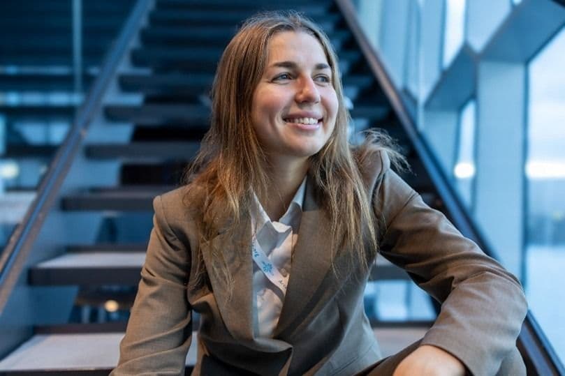 Portrett av en smilende kvinne i dressjakke som sitter i en trapp.