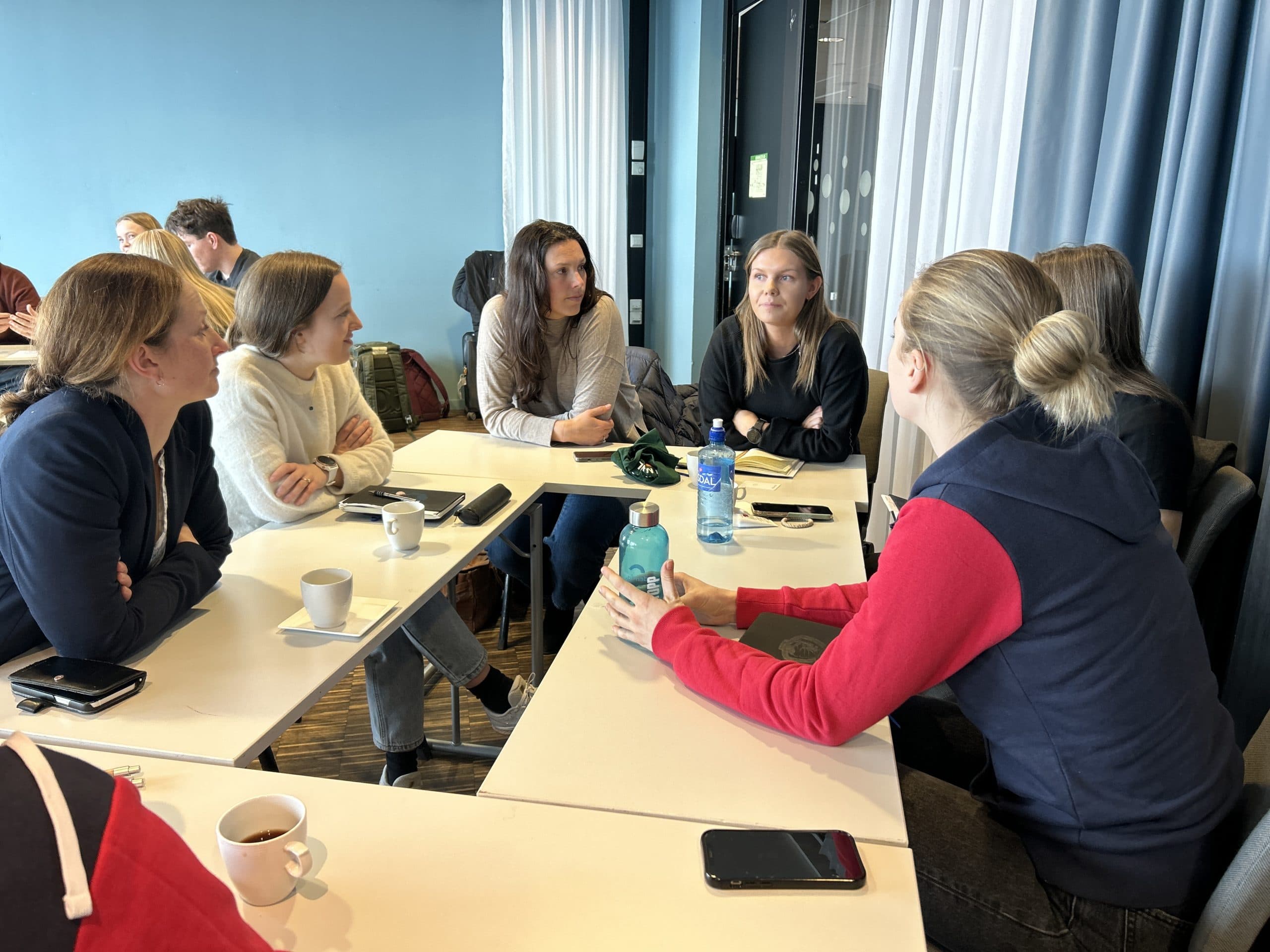En gruppe kvinner sitter rundt bord i samtale under et møte.