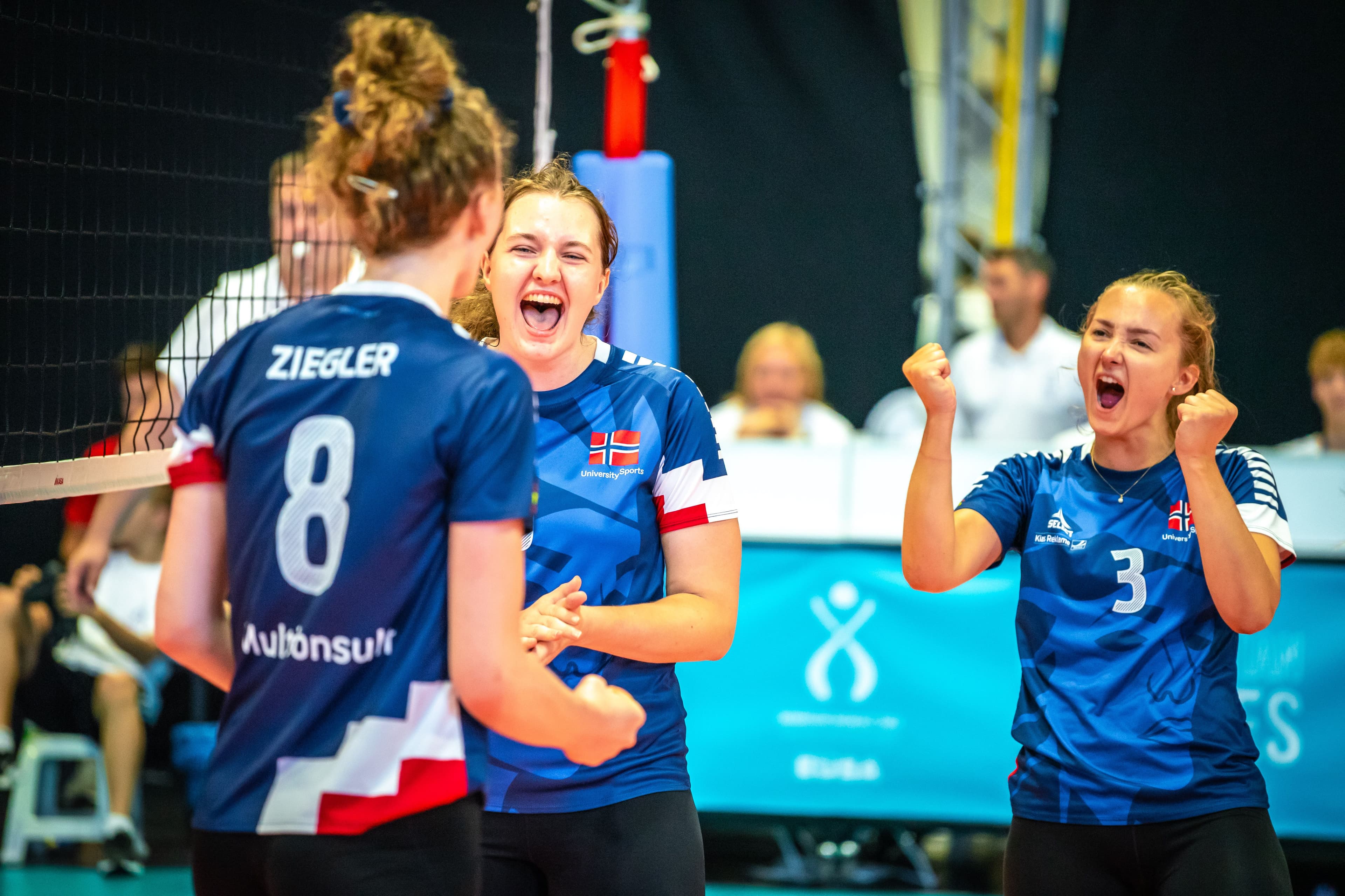 Kvinnelige volleyballspillere i norske landslagsdrakter jubler ved nettet under en kamp.
