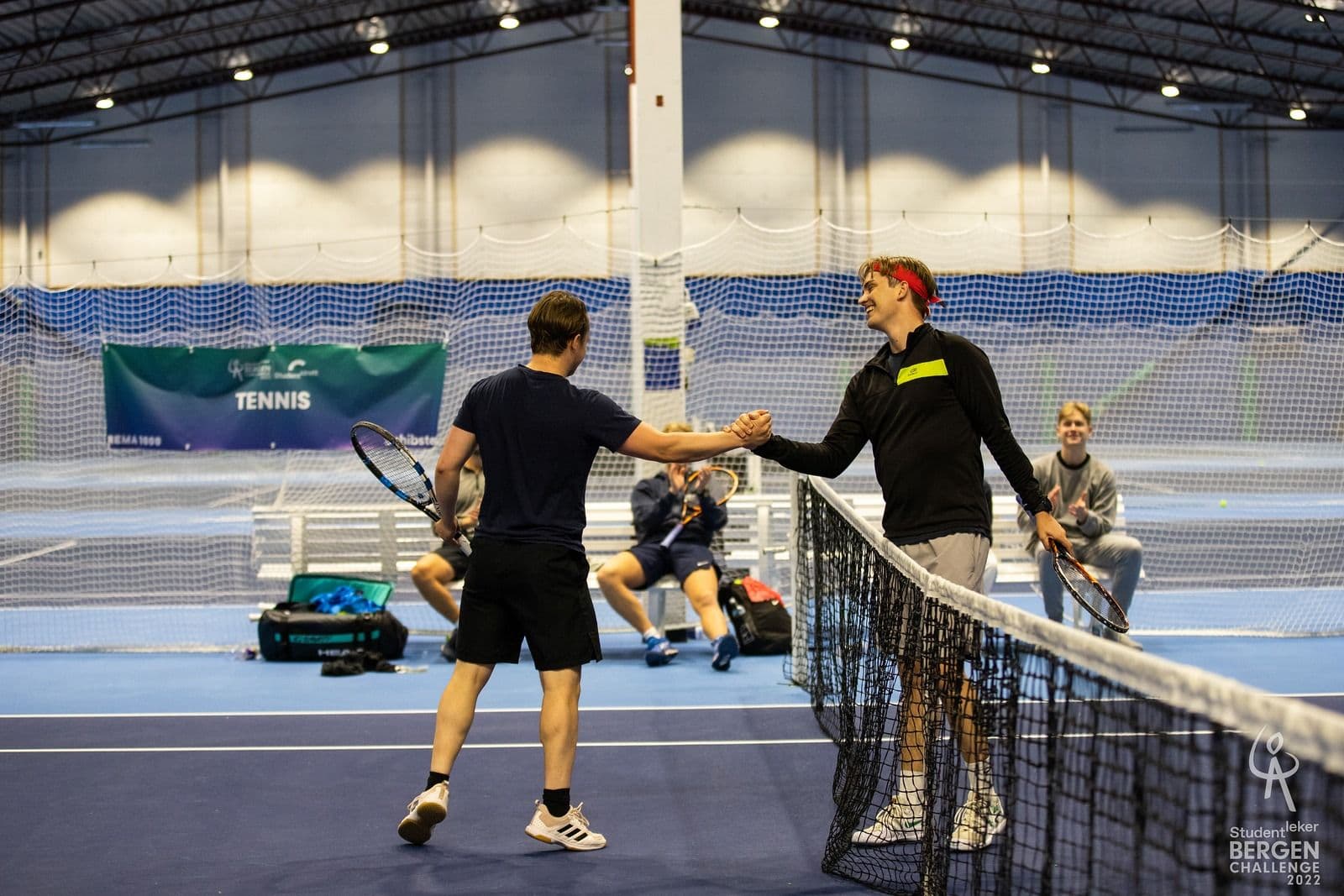 To tennisspillere håndhilser over nettet i en innendørs tennishall.